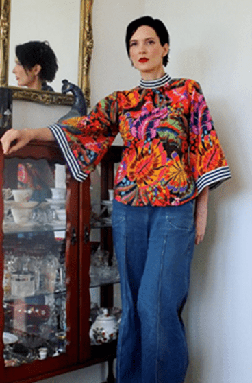 Bold tropical floral blouse featuring vibrant orange, purple, and green hues, paired with a red skirt.