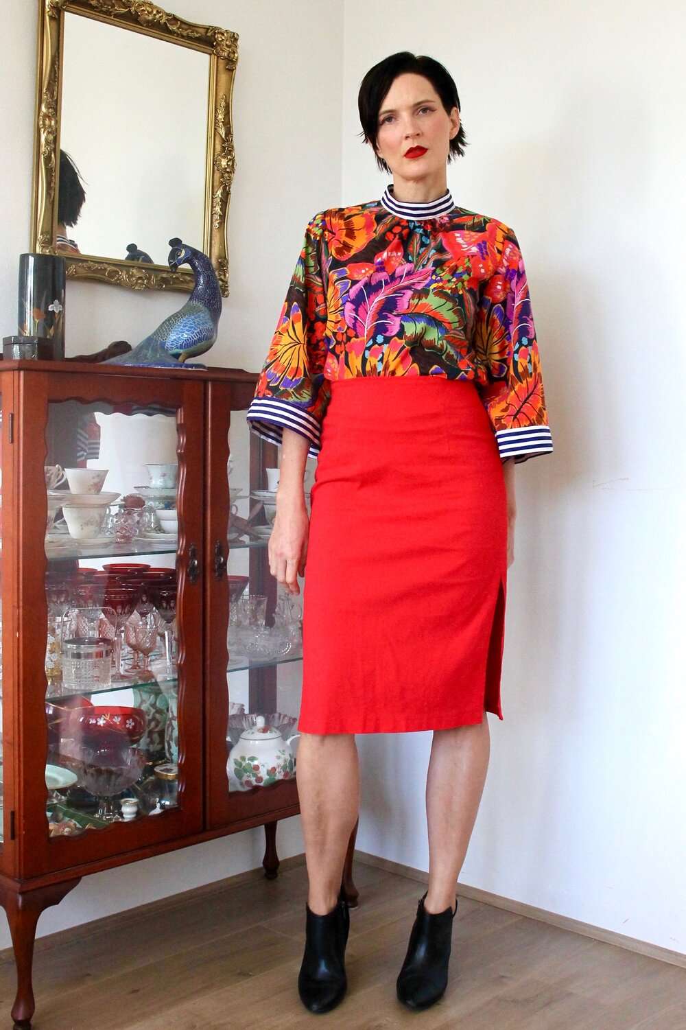 Bold tropical floral blouse featuring vibrant orange, purple, and green hues, paired with a red skirt.