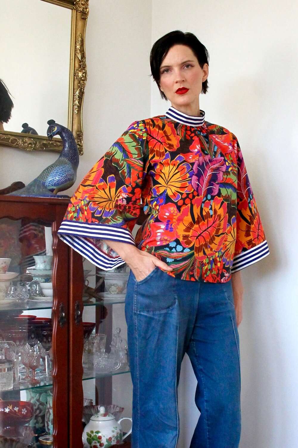 Bold tropical floral blouse featuring vibrant orange, purple, and green hues, paired with a red skirt.