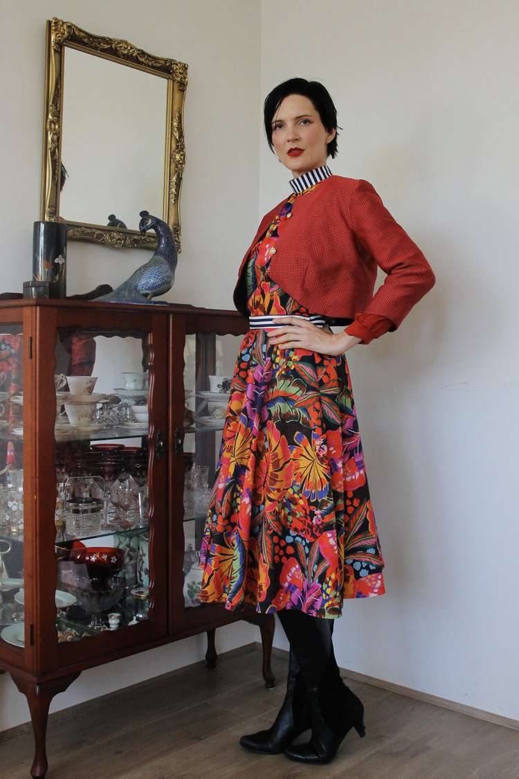 Floral patterned full-skirt dress in bold tropical colors with a red cropped jacket with fine polka dots,