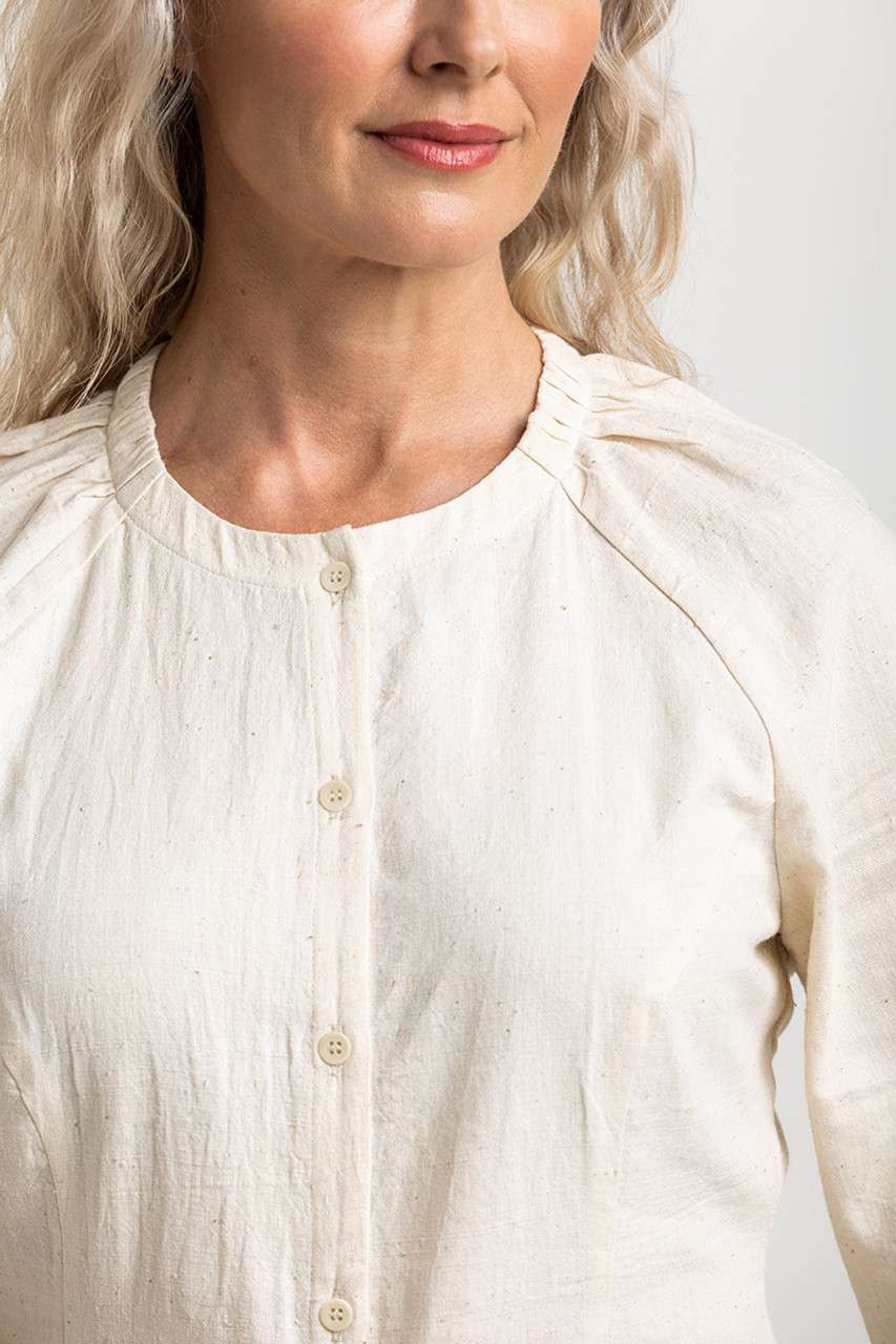 a cream, button-down top with subtle pleating at the shoulders, embodying a simple, sustainable style from Colouron Cotton.