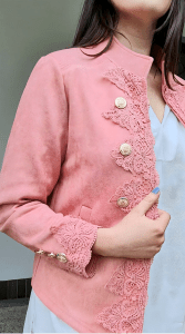 Austere Suede Touch Jacket in pink , featuring intricate lace detailing along the front and cuffs, adorned with gold buttons for a refined, elegant finish.
