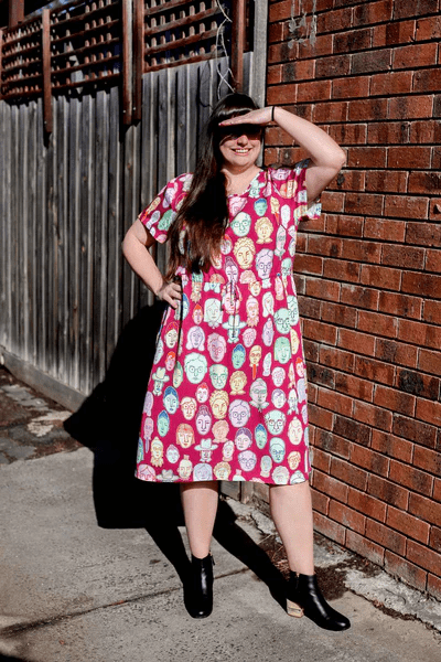Woman in a bright red dress adorned with multi-colored abstract face patterns, standing confidently against a brick wall for a vibrant, artsy street-style vibe.Christmas haul