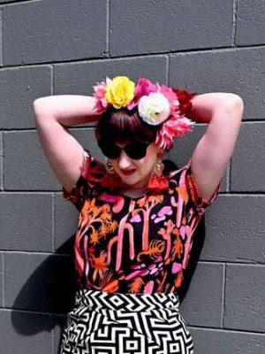 Woman wearing a vibrant black top with a pink and orange desert-themed print, posed against a similarly themed background, emphasizing the bold, artistic nature of Strebor's style. Designed by Australian designer brand Streborclothing.