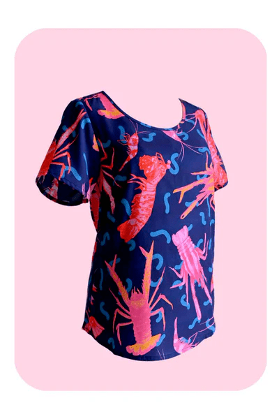 A close-up view of a textile print depicting pink and red crustaceans, including lobsters and shrimp, on a deep blue background, with wavy line details that give a playful, underwater feel. Designed by Australian designer brand Streborclothing.