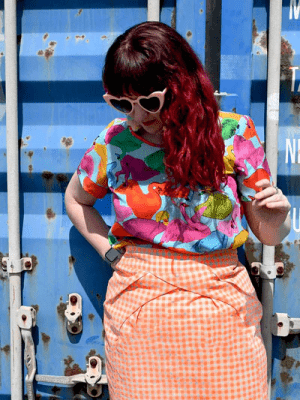 A colorful top displaying an abstract pattern of vibrant swans in reds, greens, and pinks, against a light blue background, with each swan in a unique position, adding movement and whimsy. Designed by Australian designer brand Streborclothing.