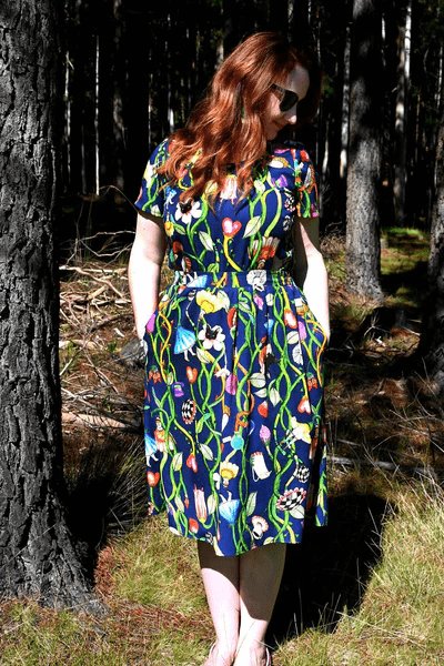 Woman in a forest scene wearing a dark blue dress with a lively floral and vine print, blending earthy elements with an artistic twist in nature-inspired surroundings. Designed by Australian designer brand Streborclothing.
