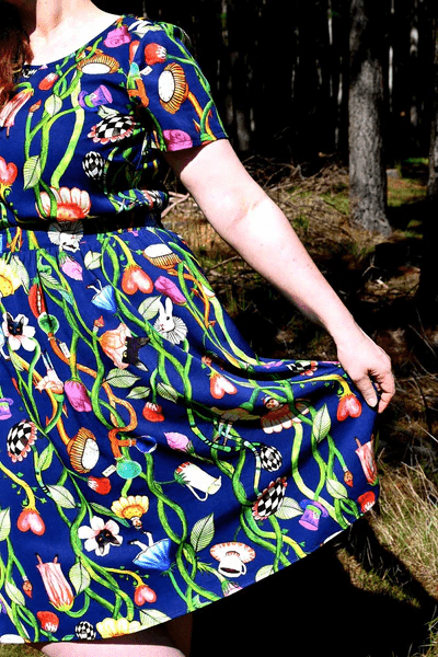 Woman in a forest scene wearing a dark blue dress with a lively floral and vine print, blending earthy elements with an artistic twist in nature-inspired surroundings. Designed by Australian designer brand Streborclothing.
