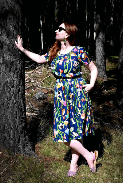 Woman in a forest scene wearing a dark blue dress with a lively floral and vine print, blending earthy elements with an artistic twist in nature-inspired surroundings. Designed by Australian designer brand Streborclothing.
