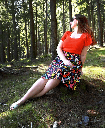 The skirt features a vibrant mushroom pattern with various brightly colored mushrooms in red, yellow, blue, pink, and green on a black background. This playful design adds a whimsical and organic feel to the outfit. Designed by Australian designer brand Streborclothing.